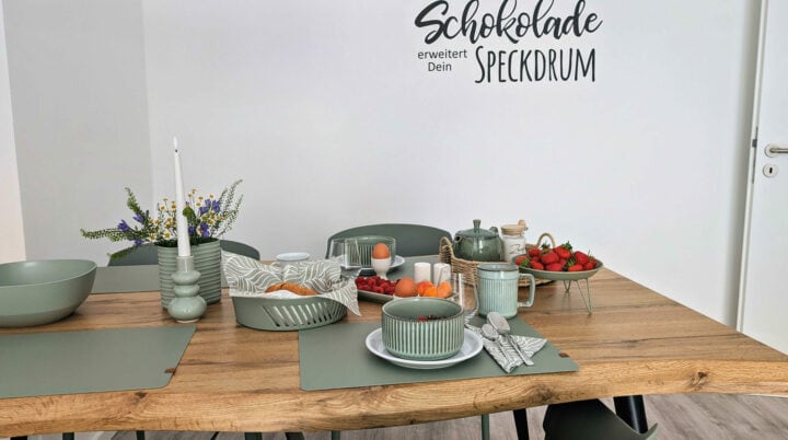MainZauber Apartments früher MainTerrasse Miltenberg am Main - Moderner Esstisch mit grünem Geschirr, Obstschalen, Teekanne und Kerze in luxuriöser Ferienwohnung in der Altstadt.
