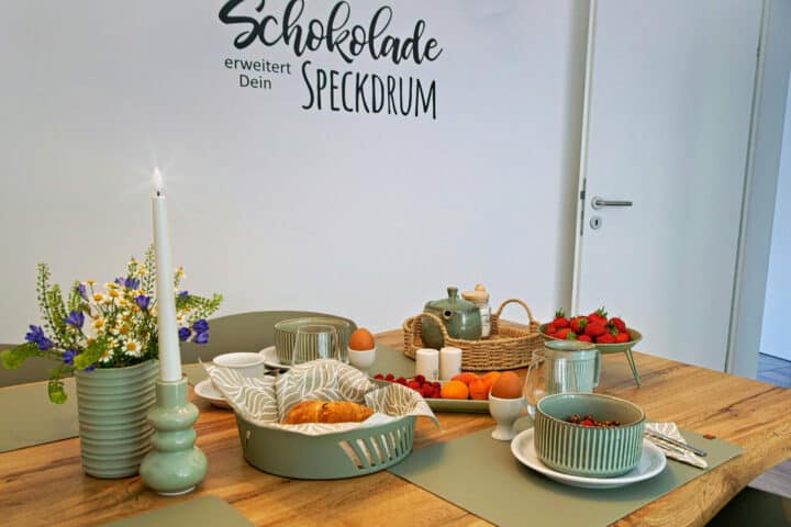 MainZauber Apartments früher MainTerrasse Miltenberg am Main - Luxuriöses Frühstück in stilvoller Ferienwohnung: Grünes Geschirr, Croissants, Obst & Deko im Altstadt-Apartment.