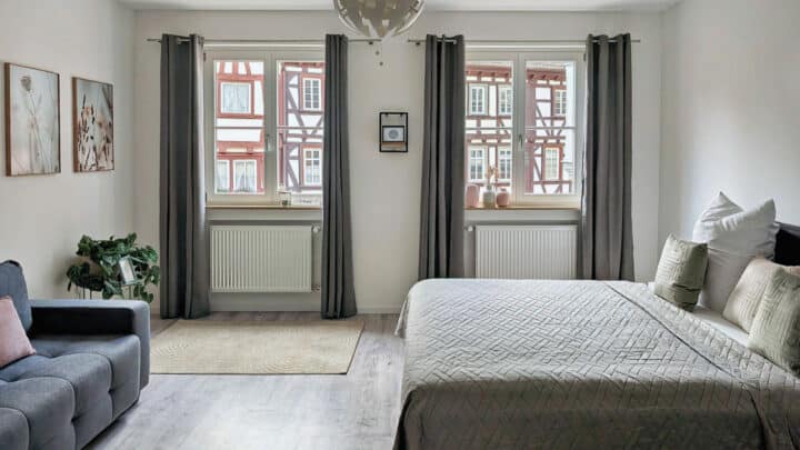 MainZauber Apartments früher MainTerrasse Miltenberg am Main - Modernes, helles Schlafzimmer in einer luxuriösen Ferienwohnung in der Altstadt mit großem Bett, Sofa und Blick auf Fachwerkhäuser.