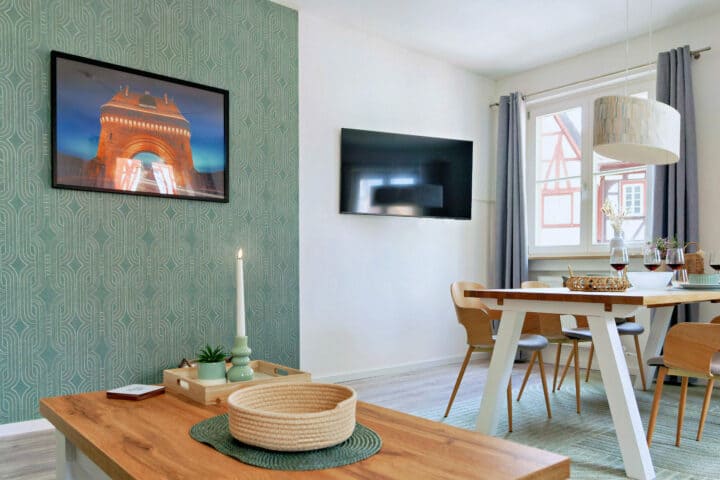 MainZauber Apartments früher MainTerrasse Miltenberg am Main - Luxuriöse Ferienwohnung in Miltenberg: Moderner Wohn-Essbereich mit Holztisch, TV, Kerze und stilvoller Akzentwand.