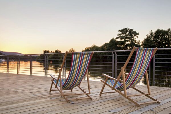 MainZauber Apartments früher MainTerrasse Miltenberg am Main - Entdecken Sie die perfekte Ferienwohnung mit atemberaubender Aussicht! Stellen Sie sich vor, Sie entspannen sich in einer luxuriösen Unterkunft auf zwei bequemen Liegestühlen auf einer Holzterrasse mit Blick auf einen ruhigen See bei Sonnenuntergang. Erleben Sie den atemberaubenden Himmel, der in warmen Farbtönen leuchtet, während sich im Hintergrund majestätische Bäume abzeichnen. Diese Luxuswohnung bietet die Bühne für Ruhe und Entspannung und bietet Ihnen einen unvergesslichen Urlaub.