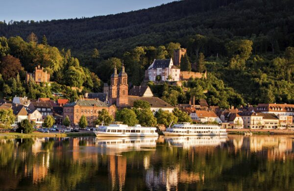 MainZauber Apartments früher MainTerrasse Miltenberg am Main - Entdecken Sie eine luxuriöse Ferienwohnung in einer malerischen Stadt an einem ruhigen Fluss. Genießen Sie atemberaubende Ausblicke und zwei charmante weiße Boote, die am Ufer vor Anker liegen. Dieses idyllische Reiseziel bietet historische Gebäude und eine wunderschöne Kirche, alles vor der Kulisse üppiger, grüner, bewaldeter Hügel unter klarem Himmel. Diese Unterkunft ist perfekt für Ihren nächsten Urlaubsaufenthalt und bietet den ultimativen Zufluchtsort für alle, die Ruhe und Geschichte in ihrer Ferienwohnung suchen.