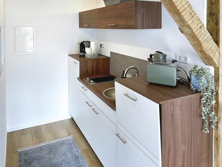 MainZauber Apartments früher MainTerrasse Miltenberg am Main - Entdecken Sie Ihre ideale Ferienwohnung mit einer eleganten, modernen Küchenzeile, die für den perfekten Kurzurlaub konzipiert wurde. Diese luxuriöse Wohnung verfügt über weiße Schränke und elegante Holzarbeitsplatten sowie wichtige Annehmlichkeiten wie Spüle, Herd, Toaster, Wasserkocher und Kaffeemaschine für Ihren Komfort. Eine bezaubernde Hängepflanze verbessert die Atmosphäre des Raums, ergänzt durch stilvolle helle Holzböden, die dieser raffinierten Umgebung einen Hauch von Wärme verleihen. Erleben Sie Komfort und Eleganz in jeder Ecke Ihres Urlaubsdomizils.