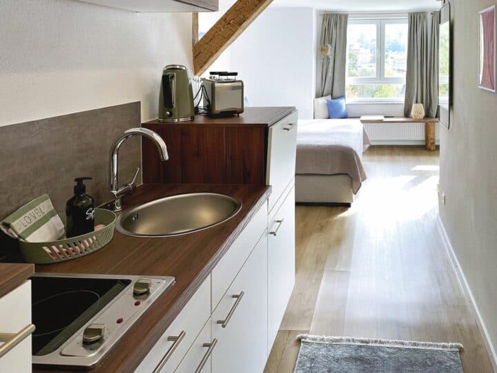 MainZauber Apartments früher MainTerrasse Miltenberg am Main - Entdecken Sie den perfekten Urlaubsort in diesem kompakten Studio-Apartment, maßgeschneidert für Reisende, die eine gemütliche und praktische Unterkunft suchen. Dieses gut ausgestattete Luxus-Apartment für den Urlaub verfügt über eine funktionale Küchenzeile mit Spüle, Elektroherd, Wasserkocher und Toaster, um Ihren Aufenthalt so angenehm wie möglich zu gestalten. Ziehen Sie sich in den sonnendurchfluteten Schlafbereich zurück, der mit hellem Boden und großen Fenstern ausgestattet ist, die den Raum mit natürlichem Licht füllen. Freuen Sie sich über zusätzliche Details wie eine grüne Seifenflasche und ein Tablett neben der Spüle. Ideal für alle, die in ihrem Urlaubserlebnis Einfachheit mit Komfort verbinden möchten.