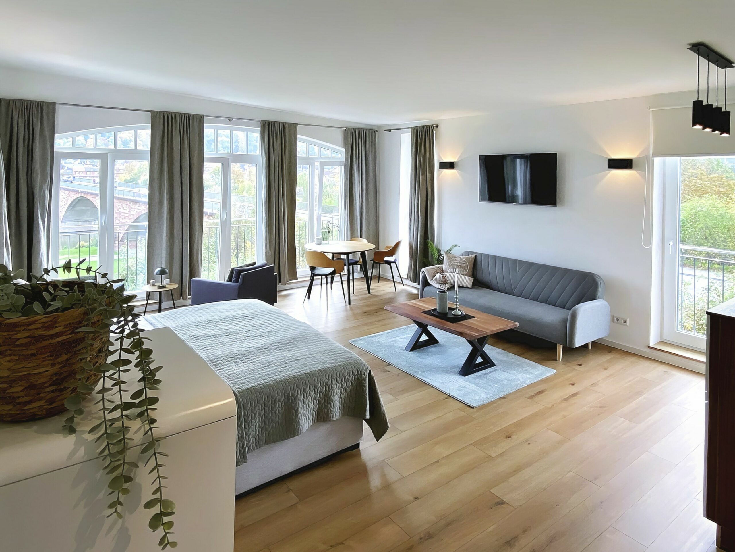MainZauber Apartments früher MainTerrasse Miltenberg am Main - Entdecken Sie die perfekte Luxus-Ferienwohnung für Ihren Urlaub! Diese atemberaubende Unterkunft bietet einen geräumigen, offenen Wohnbereich, der mühelos Komfort und Stil vereint. Entspannen Sie sich auf dem weichen dunkelgrauen Sofa oder genießen Sie Ihre Lieblingssendungen auf dem an der Wand montierten Fernseher, während Sie durch große Fenster mit eleganten Vorhängen den Blick auf üppiges Grün genießen. Der gut ausgestattete Schlafbereich sorgt für eine erholsame Nachtruhe, während der charmante Essbereich über einen schicken runden Tisch mit vier Stühlen verfügt, der sich ideal für gemütliche Mahlzeiten oder Zusammenkünfte eignet. Erleben Sie unvergleichlichen Komfort in dieser wunderschönen Ferienwohnung!