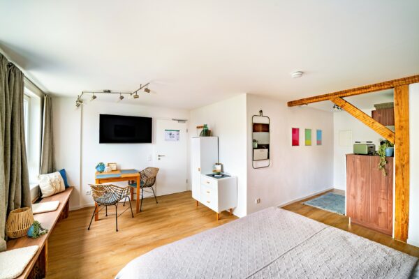 MainZauber Apartments Miltenberg am Main - Entdecken Sie die perfekte Ferienwohnung für Ihren nächsten Urlaub! Diese luxuriöse Unterkunft bietet ein helles und gemütliches Schlafzimmer, das für ultimative Entspannung konzipiert ist. Das Zimmer verfügt über ein bequemes Bett mit einer schicken beigen Steppdecke, ergänzt durch elegante Holzakzente. Ein praktischer Schreibtisch mit Stuhl bietet Platz für alle Arbeits- oder Freizeitaktivitäten, während ein an der Wand montierter Fernseher für Unterhaltung auf Knopfdruck sorgt. Genießen Sie das natürliche Licht, das durch das Fenster fällt, während Sie auf der stilvollen Holzbank entspannen. Das moderne Design wird durch lebendige Wandkunst und üppige Topfpflanzen aufgewertet und schafft eine einladende Atmosphäre in Ihrer Luxuswohnung für den Urlaub. Sorgen Sie dafür, dass Ihr Aufenthalt mit unseren außergewöhnlichen Unterkünften unvergesslich wird!