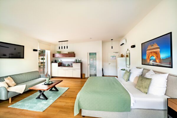 MainZauber Apartments Miltenberg am Main - Erleben Sie den ultimativen Kurzurlaub in dieser luxuriösen Ferienwohnung, in der modernes Design auf Komfort trifft. Diese elegant gestaltete Unterkunft verfügt über ein luftiges Schlafzimmer mit einer flauschigen grünen Tagesdecke, ergänzt durch ein stilvolles graues Sofa und einen schicken Couchtisch aus Holz, perfekt zum Entspannen. Genießen Sie Ihre Lieblingssendungen auf dem an der Wand montierten Fernseher vor makellos weißen Wänden, die mit geschmackvollen Kunstwerken geschmückt sind. Die kompakte, aber voll ausgestattete Küche sorgt dafür, dass Sie während Ihres Aufenthalts alles haben, was Sie zum Zubereiten von Mahlzeiten benötigen. Genießen Sie das natürliche Licht, das den Raum durchflutet und eine warme und einladende Atmosphäre schafft, in die Sie nach der Erkundung Ihres Reiseziels gerne zurückkehren werden.