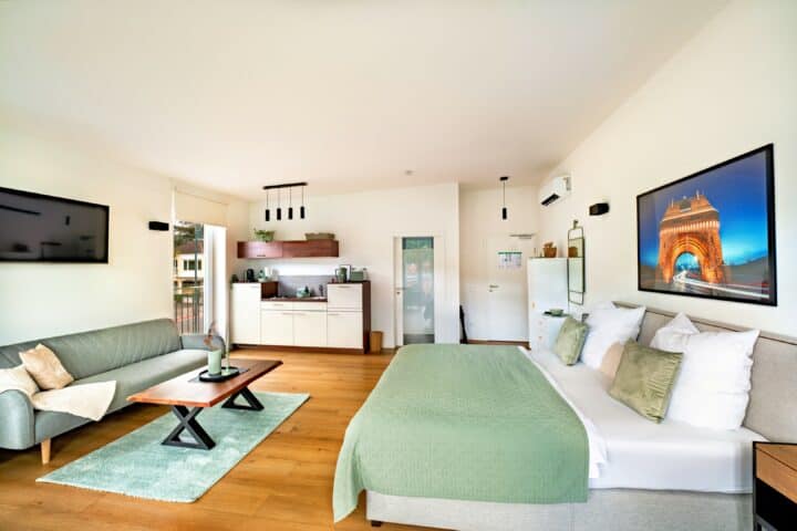 MainZauber Apartments Miltenberg am Main - Erleben Sie den ultimativen Kurzurlaub in dieser luxuriösen Ferienwohnung, in der modernes Design auf Komfort trifft. Diese elegant gestaltete Unterkunft verfügt über ein luftiges Schlafzimmer mit einer flauschigen grünen Tagesdecke, ergänzt durch ein stilvolles graues Sofa und einen schicken Couchtisch aus Holz, perfekt zum Entspannen. Genießen Sie Ihre Lieblingssendungen auf dem an der Wand montierten Fernseher vor makellos weißen Wänden, die mit geschmackvollen Kunstwerken geschmückt sind. Die kompakte, aber voll ausgestattete Küche sorgt dafür, dass Sie während Ihres Aufenthalts alles haben, was Sie zum Zubereiten von Mahlzeiten benötigen. Genießen Sie das natürliche Licht, das den Raum durchflutet und eine warme und einladende Atmosphäre schafft, in die Sie nach der Erkundung Ihres Reiseziels gerne zurückkehren werden.