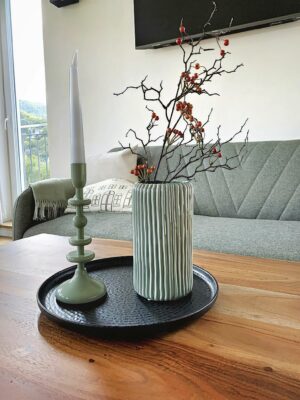 Entdecken Sie mit unseren luxuriösen Unterkünften das perfekte Urlaubsapartment. Dieser elegante Raum verfügt über ein modernes Wohnzimmer mit einem stilvollen Holztisch, der mit einer dekorativen Vase voller Zweige und roter Beeren geschmückt ist. Verbessern Sie Ihr Entspannungserlebnis mit der Atmosphäre eines grünen Kerzenständers mit einer weißen Kerze, alles elegant arrangiert auf einem eleganten schwarzen Tablett. Entspannen Sie sich auf dem plüschigen grauen Sofa, während natürliches Licht durch das große Fenster hereinströmt und eine einladende und ruhige Atmosphäre für Ihren Urlaubsort schafft. Egal, ob Sie Komfort oder Stil suchen, dieses luxuriöse Urlaubsapartment verspricht, Ihren Aufenthalt zu verbessern. - MainZauber Apartments Miltenberg am Main