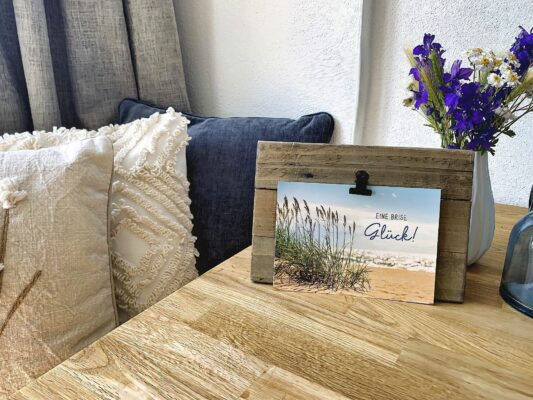 Entdecken Sie die perfekte Ferienwohnung mit warmer und einladender Atmosphäre für Ihren Urlaub. Erleben Sie eine luxuriöse Unterkunft mit einem gemütlichen Interieur, das mit dekorativen Kissen auf einem bequemen Sofa und einem eleganten Tisch aus Holz geschmückt ist. Verschönern Sie Ihren Aufenthalt mit charmanten Details wie einem Holzrahmen mit der Aufschrift „Eine Brise Glück!“ neben einer Vase mit leuchtend violetten Blumen und machen Sie dies zur idealen Luxuswohnung für Ihren unvergesslichen Urlaub. - MainZauber Apartments Miltenberg am Main