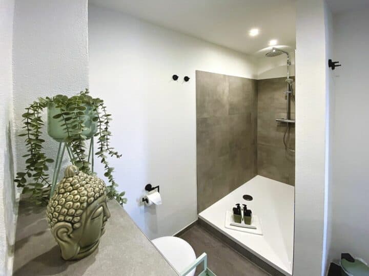 MainZauber Apartments früher MainTerrasse Miltenberg am Main - Entdecken Sie das perfekte Urlaubserlebnis in der Ferienwohnung Miltenberg, wo Luxus auf modernes Design trifft. Diese exquisite Unterkunft verfügt über ein elegantes Badezimmer mit ebenerdiger Dusche im Betonstil und luxuriösen Toilettenartikeln. Genießen Sie die beruhigende Note einer Topfpflanze und einer Buddhakopf-Dekoration, die zur Atmosphäre beitragen. Die minimalistischen Akzente, darunter makellos weiße Wände und elegante Einbauleuchten, schaffen eine beruhigende MainMoment-Atmosphäre für Ihren unvergesslichen Aufenthalt.