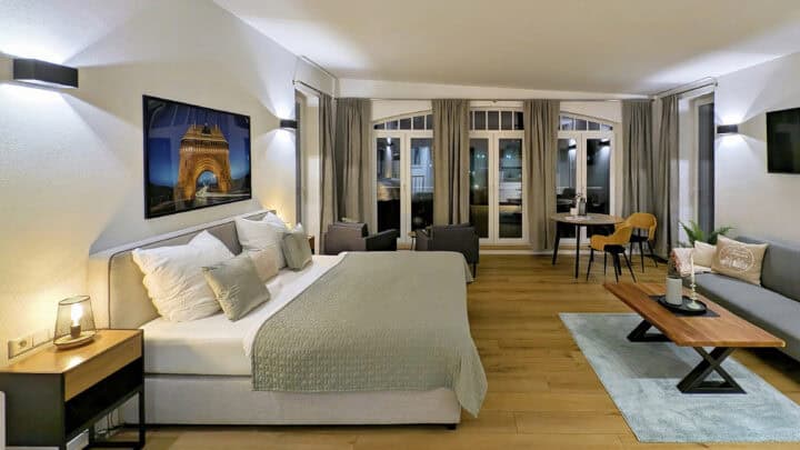 MainZauber Apartments früher MainTerrasse Miltenberg am Main - Entdecken Sie mit diesem modernen, gut beleuchteten Apartment-Schlafzimmer das ultimative Luxus-Feriendomizil. Dieses Ferienapartment ist perfekt für Reisende, die einen anspruchsvollen Urlaub verbringen möchten. Es verfügt über ein geräumiges Schlafzimmer mit einem großen, weichen Bett mit eleganter grüner Bettwäsche. Entspannen Sie sich im einladenden Wohnbereich mit einem bequemen Sofa und einem stilvollen Couchtisch sowie stimmungsvollen Kerzen. Genießen Sie Ihre Mahlzeiten in der gemütlichen Essecke und genießen Sie dabei das natürliche Licht, das durch die großen, mit hellen Vorhängen behangenen Fenster strömt. Atemberaubende Wandkunst und moderne Beleuchtung tragen zur gemütlichen Atmosphäre dieses außergewöhnlichen Luxusapartments für Ihren nächsten unvergesslichen Urlaub bei.