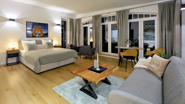 MainZauber Apartments früher MainTerrasse Miltenberg am Main - Entdecken Sie den perfekten Urlaubsort in diesem luxuriösen Apartment mit einem modernen und geräumigen Schlafzimmer. Genießen Sie eine erholsame Nachtruhe auf dem großen, bequemen Bett, ergänzt durch ein elegantes graues Sofa und einen eleganten Couchtisch aus Holz zum Entspannen. Die Unterkunft bietet einen einladenden kleinen Essbereich mit stilvollen Stühlen vor atemberaubenden raumhohen Fenstern mit schicken grauen Vorhängen, die einen atemberaubenden Ausblick bieten. Tauchen Sie ein in das künstlerische Ambiente mit sorgfältig kuratierten Kunstwerken an den Wänden. Glänzende Holzböden verleihen dem Raum Wärme, während sanfte Beleuchtung eine ruhige Atmosphäre für Ihren Urlaub schafft. Dieses Luxusapartment ist ideal für diejenigen, die erstklassige Ferienvermietungserlebnisse suchen, und wurde entworfen, um Ihren Aufenthalt unvergesslich zu machen.