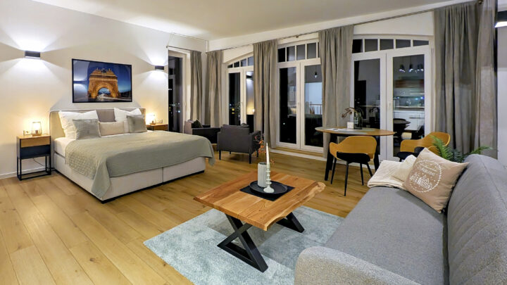 MainZauber Apartments früher MainTerrasse Miltenberg am Main - Entdecken Sie den perfekten Urlaubsort in diesem luxuriösen Apartment mit einem modernen und geräumigen Schlafzimmer. Genießen Sie eine erholsame Nachtruhe auf dem großen, bequemen Bett, ergänzt durch ein elegantes graues Sofa und einen eleganten Couchtisch aus Holz zum Entspannen. Die Unterkunft bietet einen einladenden kleinen Essbereich mit stilvollen Stühlen vor atemberaubenden raumhohen Fenstern mit schicken grauen Vorhängen, die einen atemberaubenden Ausblick bieten. Tauchen Sie ein in das künstlerische Ambiente mit sorgfältig kuratierten Kunstwerken an den Wänden. Glänzende Holzböden verleihen dem Raum Wärme, während sanfte Beleuchtung eine ruhige Atmosphäre für Ihren Urlaub schafft. Dieses Luxusapartment ist ideal für diejenigen, die erstklassige Ferienvermietungserlebnisse suchen, und wurde entworfen, um Ihren Aufenthalt unvergesslich zu machen.