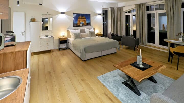 MainZauber Apartments früher MainTerrasse Miltenberg am Main - Entdecken Sie mit diesem luxuriösen, modernen Studio-Apartment die ultimative Urlaubsunterkunft. Dieses geräumige Studio ist perfekt für Ihren nächsten Urlaub. Es verfügt über atemberaubende Holzböden und bietet einen gemütlichen Schlafbereich mit einem weichen Bett, Nachttischen, einer schicken Kommode und einem eleganten Wandspiegel. Entspannen Sie sich im bequemen Sitzbereich mit stilvollen Sesseln und einem hölzernen Couchtisch, der durch große Fenster mit eleganten Vorhängen in natürliches Licht getaucht ist. Machen Sie es zu Ihrem idealen zweiten Zuhause in Ihrem nächsten Urlaub!