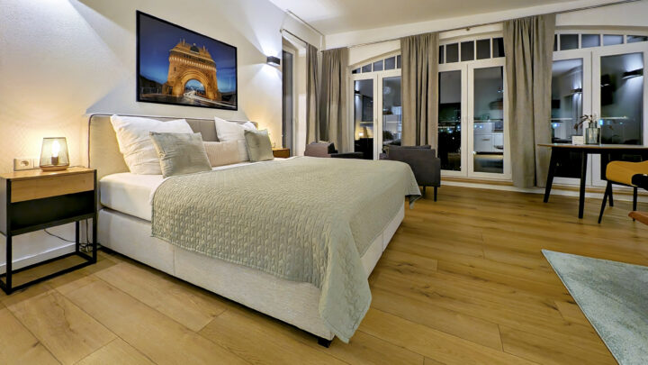 MainZauber Apartments früher MainTerrasse Miltenberg am Main - Entdecken Sie Ihre ideale Ferienwohnung, die die perfekte Mischung aus Komfort und Stil bietet. Diese luxuriöse Unterkunft verfügt über ein geräumiges Schlafzimmer mit einem weichen Bett mit einer eleganten grünen Bettdecke, das erholsame Nächte verspricht. Genießen Sie die Kunstfertigkeit über dem Bett und entspannen Sie sich im sanften Schein einer Lampe auf einem eleganten Nachttisch aus Holz. Die Wohnung verfügt über schöne Holzböden und große Fenster mit stilvollen Vorhängen, die Ihren Aufenthalt verschönern. Entspannen Sie sich im durchdacht gestalteten Sitzbereich und machen Sie diese Luxuswohnung zu Ihrem perfekten Rückzugsort für ein exquisites Urlaubserlebnis.
