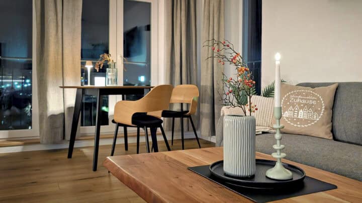 MainZauber Apartments früher MainTerrasse Miltenberg am Main - Entdecken Sie das perfekte Luxusapartment für den Urlaub mit einem gemütlichen Wohnbereich, der alles bietet, was Sie für einen erholsamen Urlaub brauchen. Diese einladende Unterkunft verfügt über ein stilvolles Wohnzimmer mit einem Holztisch und Stühlen, die neben großen Fenstern stehen und schönes Tageslicht hereinlassen. Die durchdachte Dekoration umfasst eine Kerze, eine Vase und eine Pflanze, die das Ambiente dieses charmanten Raums verbessern. Entspannen Sie auf dem bequemen Sofa mit dekorativen Kissen mit einzigartigen Hausdesigns. Erleben Sie Wärme und Gelassenheit in einem exquisiten Ferienapartment, das Ihren Urlaub unvergesslich machen soll.