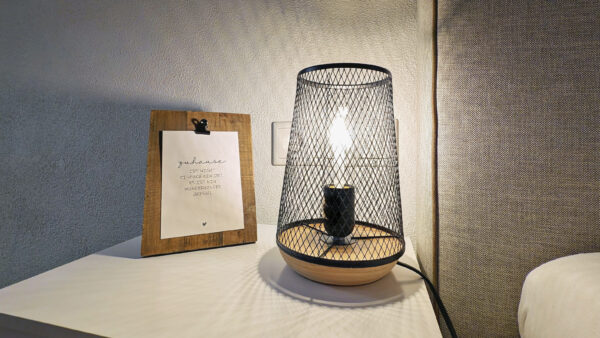 MainZauber Apartments früher MainTerrasse Miltenberg am Main - Erleben Sie die perfekte Mischung aus Stil und Komfort in Ihrer Ferienwohnung. Diese luxuriöse Ferienwohnung verfügt über eine moderne Nachttischlampe mit einem schicken Schirm aus Drahtgeflecht, die ein warmes Licht in den Raum bringt. Neben der Lampe befindet sich ein wunderschön gearbeiteter Holzrahmen mit einem eleganten Zitat, der auf einem makellos weißen Nachttisch ruht und eine einladende und anspruchsvolle Atmosphäre für Ihren Urlaubsort schafft.