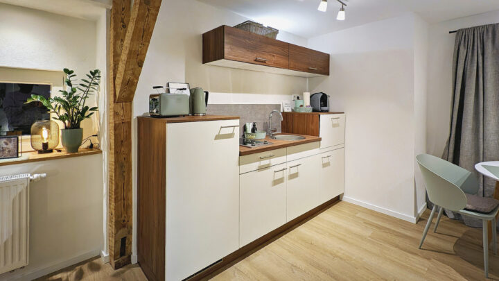 MainZauber Apartments früher MainTerrasse Miltenberg am Main - Erleben Sie den Inbegriff von Komfort und Stil in unserer luxuriösen Ferienwohnung, die perfekt darauf ausgelegt ist, Ihren Aufenthalt zu verschönern. Diese exquisite Unterkunft verfügt über eine moderne Küchenzeile mit eleganten weißen Schränken und edlen Holzakzenten, die mit allen wichtigen Geräten für mühelosen Komfort ausgestattet ist. Verbessern Sie Ihr kulinarisches Erlebnis in einem Raum, der durch natürliches Licht von Fenstervorhängen bereichert wird. Machen Sie es sich am eleganten Esstisch, umgeben von schicken weißen Stühlen, gemütlich, während Holzbalken und heller Holzboden der Wohnung Wärme und Charme verleihen. Ideal für alle, die eine erstklassige Ferienwohnung suchen, die modernen Komfort nahtlos mit einladender Ästhetik verbindet.