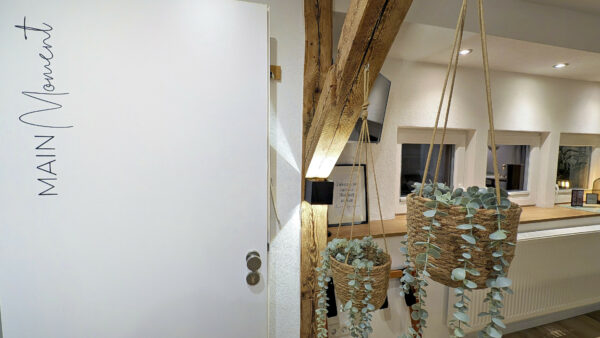 MainZauber Apartments früher MainTerrasse Miltenberg am Main - Entdecken Sie Ihre ideale Ferienwohnung mit charmanter, gemütlicher Inneneinrichtung, die einen unvergesslichen Aufenthalt verspricht. Diese luxuriöse Ferienwohnung verfügt über hängende Pflanzkübel mit herabhängendem Grün, die Ihrer Unterkunft einen Hauch von Natur verleihen. Rustikale Holzbalken harmonieren perfekt mit moderner Ästhetik, während die elegante weiße Tür mit der Aufschrift „Main Moment“ Sie in einen ruhigen Raum einlädt. Genießen Sie den Komfort einer stilvollen Theke und genießen Sie das natürliche Licht, das durch die beleuchteten Fenster strömt. Ihr Traumurlaub erwartet Sie in dieser exquisiten Luxuswohnung, die nur für Sie entworfen wurde!