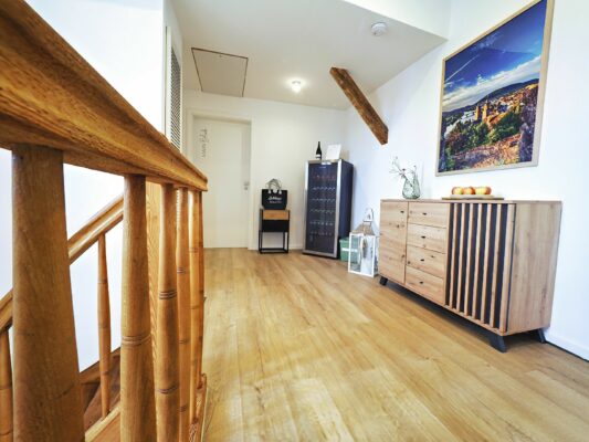 Treten Sie ein in die Ferienwohnung Ihrer Träume, wo Sie ein moderner und heller Flur mit einer eleganten Holztreppe und einem schicken Sideboard begrüßt. Dieser exquisite Raum, der sich perfekt für Ihren Luxusapartmenturlaub eignet, verfügt über einen praktischen Weinkühlschrank, der Ihren Aufenthalt noch schöner macht. Die makellos weiße Wand ziert ein atemberaubendes Landschaftskunstwerk, begleitet von einer stilvollen Anordnung frischer Blumen in einer Vase und einer Schale mit Äpfeln auf dem Sideboard – jedes Detail ist für eine unvergessliche Urlaubsunterkunft konzipiert. - MainZauber Apartments Miltenberg am Main