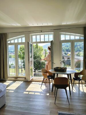 Stellen Sie sich vor, Sie stehen auf dem Balkon einer luxuriösen Ferienwohnung und genießen die atemberaubende Aussicht auf einen ruhigen Fluss und sanfte Hügel. Diese stilvolle Unterkunft verfügt über große Fenster, die einen atemberaubenden Panoramablick bieten und natürliches Licht in das gemütliche Interieur bringen. Genießen Sie köstliche Mahlzeiten an Ihrem runden Esstisch mit vier bequemen Stühlen, alles vor eleganten Hartholzböden. Genießen Sie die perfekte Mischung aus Komfort und Ruhe in Ihrem Traumurlaubsort. - MainZauber Apartments Miltenberg am Main