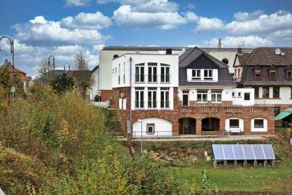 MainZauber Apartments früher MainTerrasse Miltenberg am Main - Entdecken Sie Ihr Traum-Luxus-Ferienapartment, eingebettet in einen malerischen Grashang. Diese exquisite Unterkunft in Weiß und Braun verfügt über große Fenster, die einen atemberaubenden Blick auf das üppige Grün bieten, das Sie umgibt. Perfekt unter einem teilweise bewölkten blauen Himmel gelegen, ist diese Oase nicht nur schön, sondern auch umweltfreundlich, wobei hochmoderne Solarmodule ihren Reiz noch verstärken. Erleben Sie unvergleichliche Entspannung und Komfort in diesem idyllischen Rückzugsort inmitten anderer charmanter Gebäude. Buchen Sie noch heute Ihr perfektes Luxusapartment für den Urlaub!